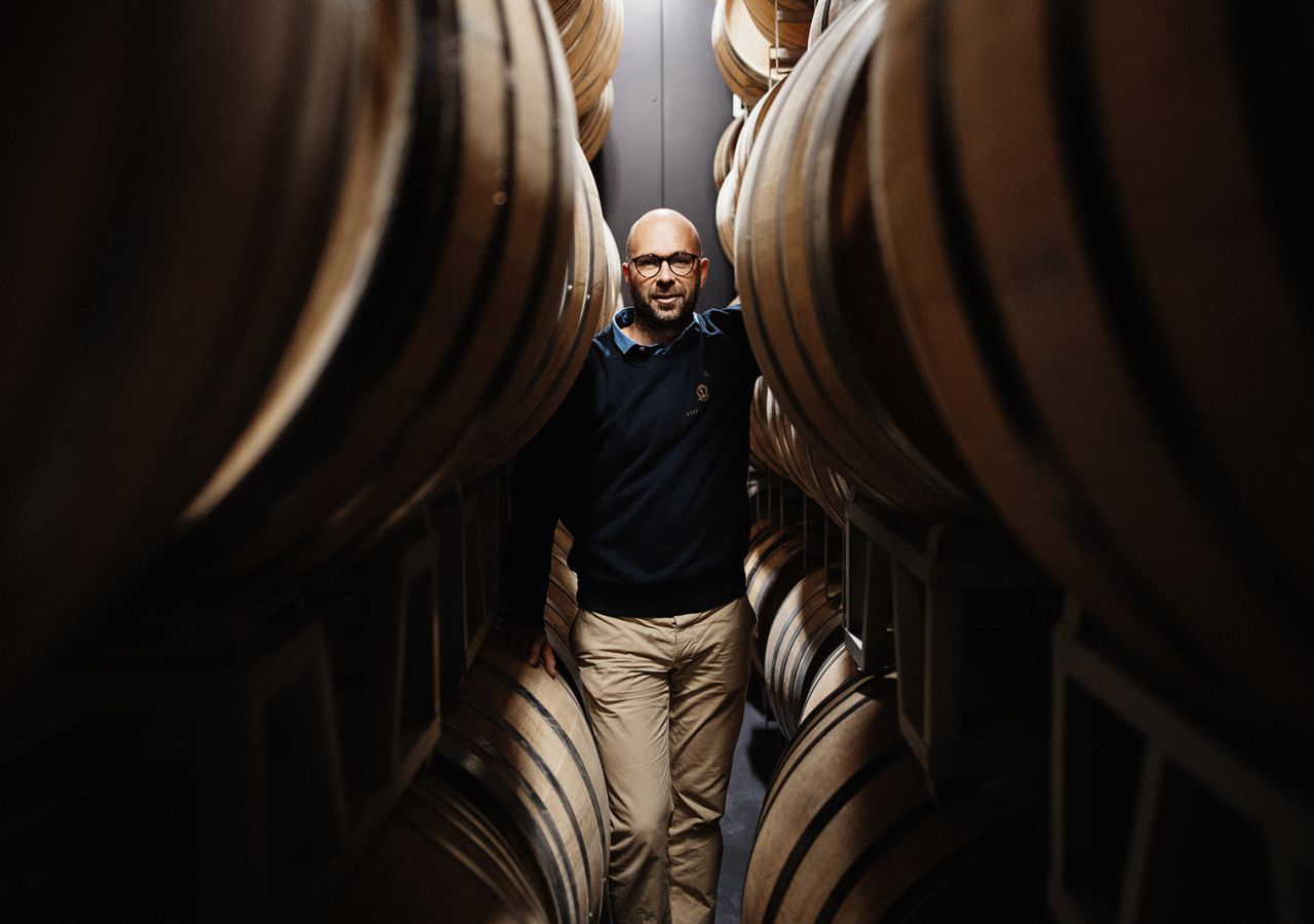 Uomo in piedi tra grandi botti di legno all’interno della cantina di Villa Saletta.